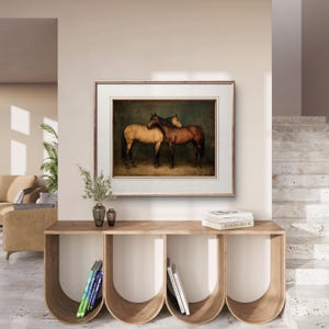 May include: A framed artwork depicts two horses, one tan and one brown, standing close together. The painting has a dark background and is displayed above a wooden console table with a curved design. The room has neutral-toned walls and a staircase.