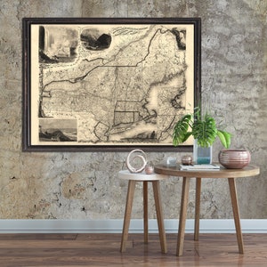 May include: A framed vintage map of New England, with a detailed illustration of the region's geography. The map is displayed on a textured concrete wall, with two small wooden side tables and decorative objects.
