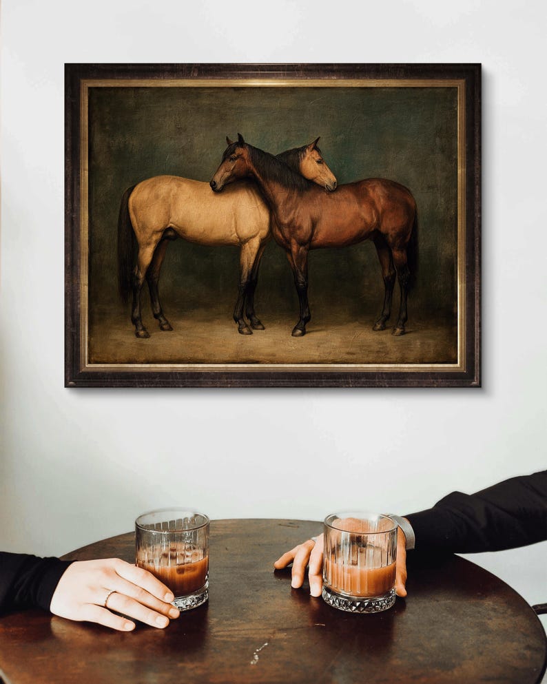 May include: A framed print featuring two horses, one tan and one brown, in a classic painting style. The horses are close together, with one resting its head on the other. The print is displayed above a table with two glasses of a brown beverage.