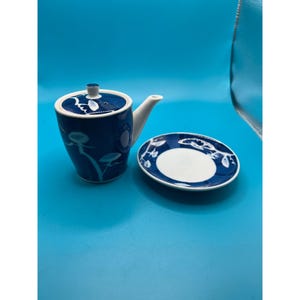May include: A small blue and white ceramic teapot with a matching saucer. The teapot has a floral design and a spout. The saucer has a similar floral design.