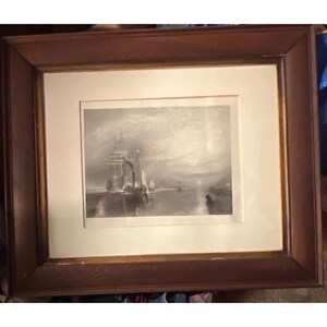 May include: A framed monochromatic print depicting a sailing ship on calm water under a hazy sky. The artwork is enclosed in a wide, dark brown wooden frame with a light-colored mat board border, creating a classic presentation for the maritime scene.