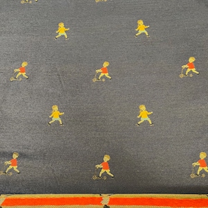 May include: Navy blue fabric with a repeating pattern of small figures riding scooters and walking. The figures are in yellow and red. A gold, red, and black striped border is at the bottom.