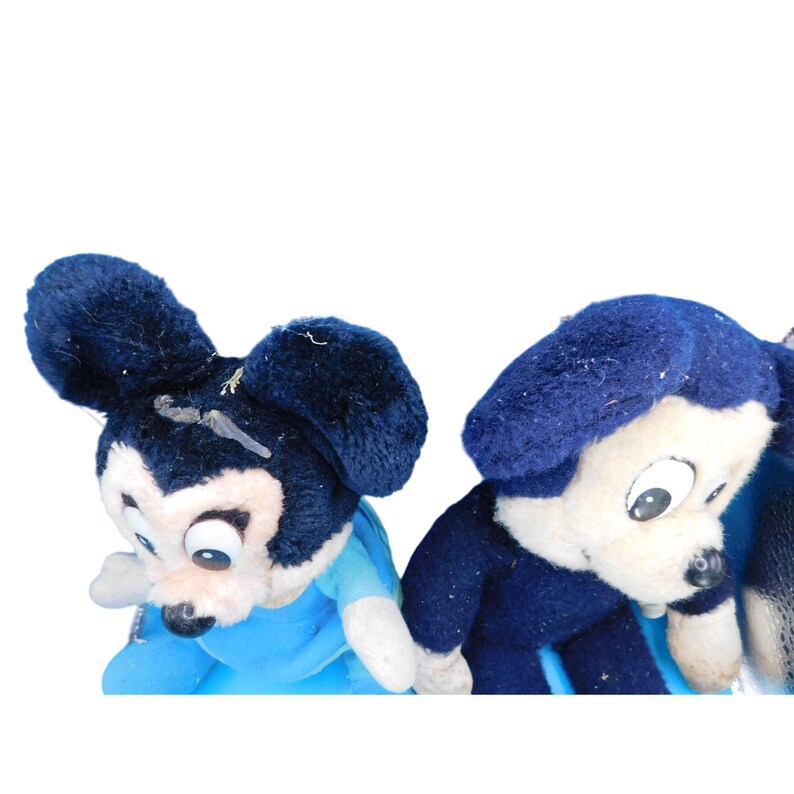 K&ouml;nnte beinhalten: Zwei Vintage-Mickey-Mouse-Pl&uuml;schtiere. Ein Mickey Mouse tr&auml;gt ein blaues Hemd, und der andere tr&auml;gt eine blaue Jacke. Beide haben schwarze Ohren und Nasen und wei&szlig;e Gesichter. Die Spielzeuge sind vor einem wei&szlig;en Hintergrund platziert.