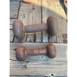 Puede incluir: Dos pesas antiguas y oxidadas con pesas de forma ovalada y un mango cilíndrico. Las pesas son de metal y muestran signos de edad y desgaste. Las pesas miden aproximadamente 25 cm de largo.