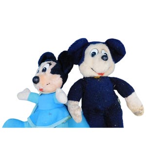 K&ouml;nnte beinhalten: Zwei Vintage-Mickey-Mouse-Pl&uuml;schtiere. Eines tr&auml;gt ein blaues Outfit, das andere ein dunkelblaues Outfit. Beide haben schwarze Ohren, wei&szlig;e Gesichter und schwarze Nasen. Die Spielzeuge sind vor einem wei&szlig;en Hintergrund platziert.