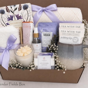 May include: A gift box containing a floral notebook, a white waffle-knit blanket with a lavender ribbon, a chocolate bar, a lavender vanilla spray, a lavender sage soak, a lavender soap, a flower-shaped candle, and a mug with two Tea With Tae packets.