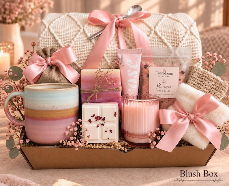 May include: A gift set in a cardboard box containing a ceramic mug with pink and tan bands, a pink ribbon-tied burlap pouch, a pink-toned soap bar, a rose-labeled tube, Everbloom Botanicals Plumeria bath salts, a wax melt, a pink candle, and a white fuzzy item.