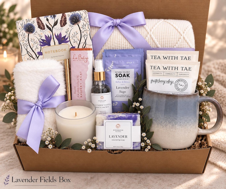 May include: A gift box containing a floral notebook, a white fuzzy towel with a lavender ribbon, a gold pen, a dark chocolate bar, a lavender vanilla spray, lavender sea salt soak, two tea bags, a white candle, and a lavender soap in a blue mug.