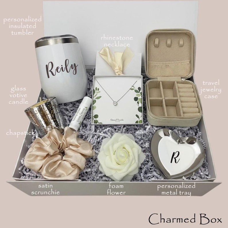May include: A gift box with a white insulated tumbler with "Reily" printed on it, a rhinestone necklace, a travel jewelry case, a glass votive candle, chapstick, a satin scrunchie, a foam flower, and a personalized metal tray.