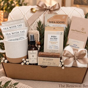 May include: A gift box containing a speckled ceramic mug with Tea With Tae packets, a bottle of Everbloom Botanicals Oat & Honey Lotion, a bar of Oat & Honey Soap, a Voesh Pedi In A Box kit, Shea-Socks, and a Moonstruck milk chocolate bar.