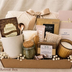 Puede incluir: Una caja de regalo que contiene una taza de cer&aacute;mica blanca, un paquete de mezcla de chocolate caliente Sorrento, una cuchara dorada, una manta de punto color crema con lazo de sat&eacute;n, un frasco de sales de ba&ntilde;o, jab&oacute;n, una vela y chocolate con leche Moonstruck.