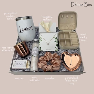 May include: A gift box with a white insulated tumbler with a name, a rose gold votive candle, a rhinestone necklace, a travel jewelry case, rose bath salts, a scrunchie, matches, and a personalized metal heart tray.