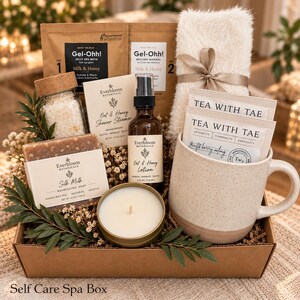 May include: A self-care spa gift box containing two Gel-Ohh! Milk & Honey packets, a fuzzy white pair of socks with a ribbon, two Tea With Tae tea bags, a speckled ceramic mug, a candle, Silk Milk soap, Oat & Honey lotion, and bath salts.