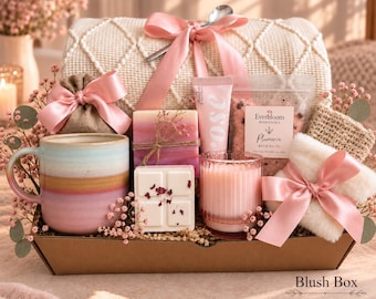 May include: A gift set in a cardboard box containing a ceramic mug with pink and tan bands, a pink ribbon-tied burlap pouch, a pink-toned soap bar, a rose-labeled tube, Everbloom Botanicals Plumeria bath salts, a wax melt, a pink candle, and a white fuzzy item.