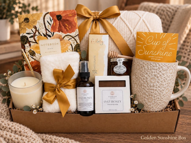 May include: A gift box containing a floral notebook, a white fuzzy cloth with a gold ribbon, a candle, a bottle of oat honey lotion, a chocolate bar, a jar of honey with a dipper, a soap bar, and a textured mug with a Cup of Sunshine card.