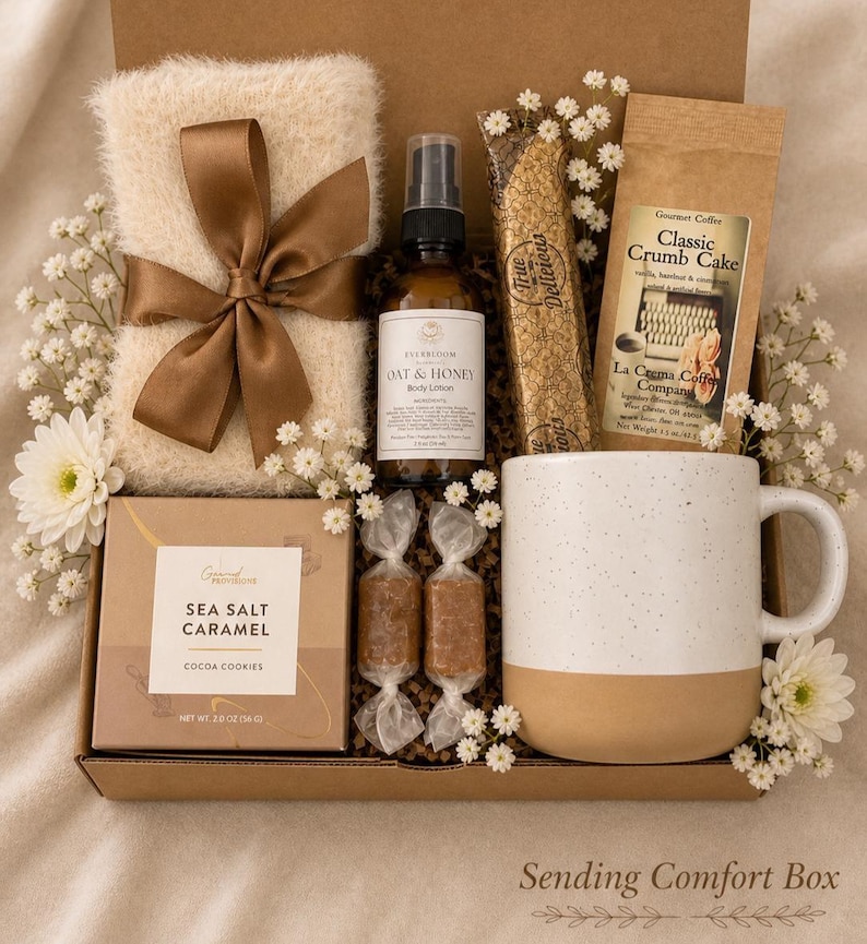 May include: A gift box containing a fuzzy cream-coloured cloth with a brown ribbon, a bottle of Oat & Honey body lotion, a package of Classic Crumb Cake coffee, a box of Sea Salt Caramel cocoa cookies, two wrapped sweets, and a speckled ceramic mug.