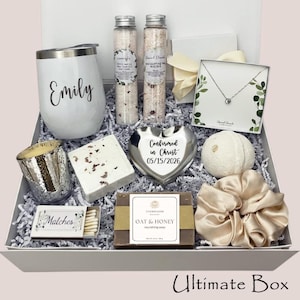 May include: A white gift box filled with various items, including a personalized tumbler, bath salts, a necklace, a candle, soap, a scrunchie, and a heart-shaped dish. The dish is engraved with "Confirmed in Christ 05/15/2026". The box is labeled "Ultimate Box".