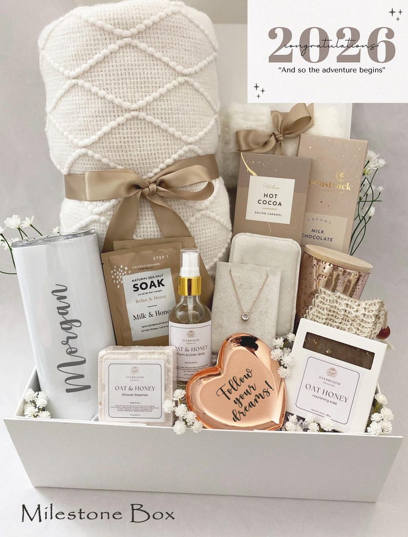 May include: A white gift box filled with self-care items, including a blanket, tumbler, chocolates, and a heart-shaped dish with the text "Follow your dreams!". The box is decorated with flowers and a ribbon.