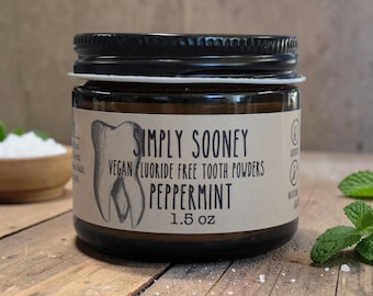 May include: A small amber glass jar with a black screw-top lid containing peppermint tooth powder. The beige label features a hand-drawn tooth illustration and the text Simply Sooney Vegan Fluoride Free Tooth Powders Peppermint 1.5 oz.