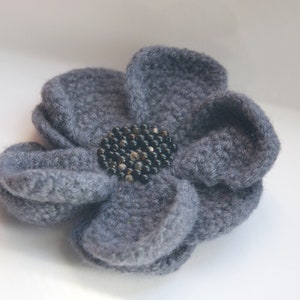 May include: A gray felt flower with a black bead center.