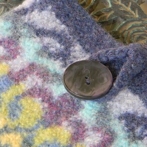 May include: A close-up of a blue and white knitted fabric with a black button. The fabric has a colourful pattern with shades of blue, white, yellow, and pink.