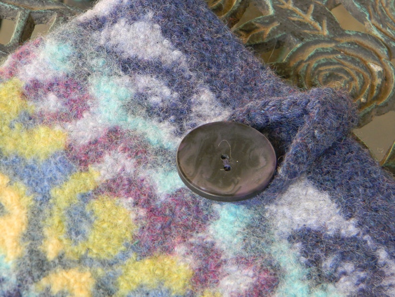 May include: A close-up of a blue and white knitted fabric with a black button. The fabric has a colourful pattern with shades of blue, white, yellow, and pink.