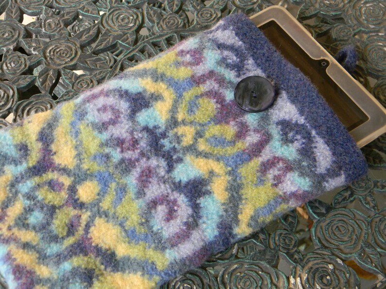 May include: A blue, yellow and purple knitted tablet sleeve with a black button closure. The sleeve is made of a soft, fuzzy material and has a geometric pattern.