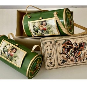 Puede incluir: Dos cajas cilíndricas verdes con ribetes dorados y diseños florales. Una caja tiene una imagen de niños en la parte delantera. La otra caja tiene una imagen de una mariposa en la parte delantera. Una tercera caja con un diseño de mariposa está cerrada.
