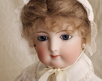 May include: A porcelain doll with blonde hair wearing a white lace bonnet and a white dress with lace trim.
