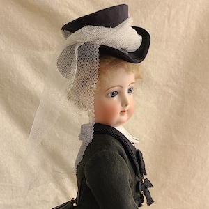 May include: A porcelain doll wearing a black velvet hat with a white veil and a black jacket with gold buttons.