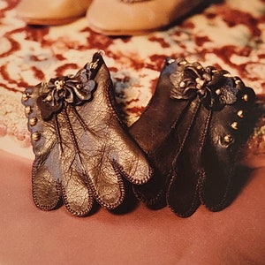 May include: A pair of brown leather gloves with decorative stitching and gold accents. The gloves have a flower design on the back of the hand.