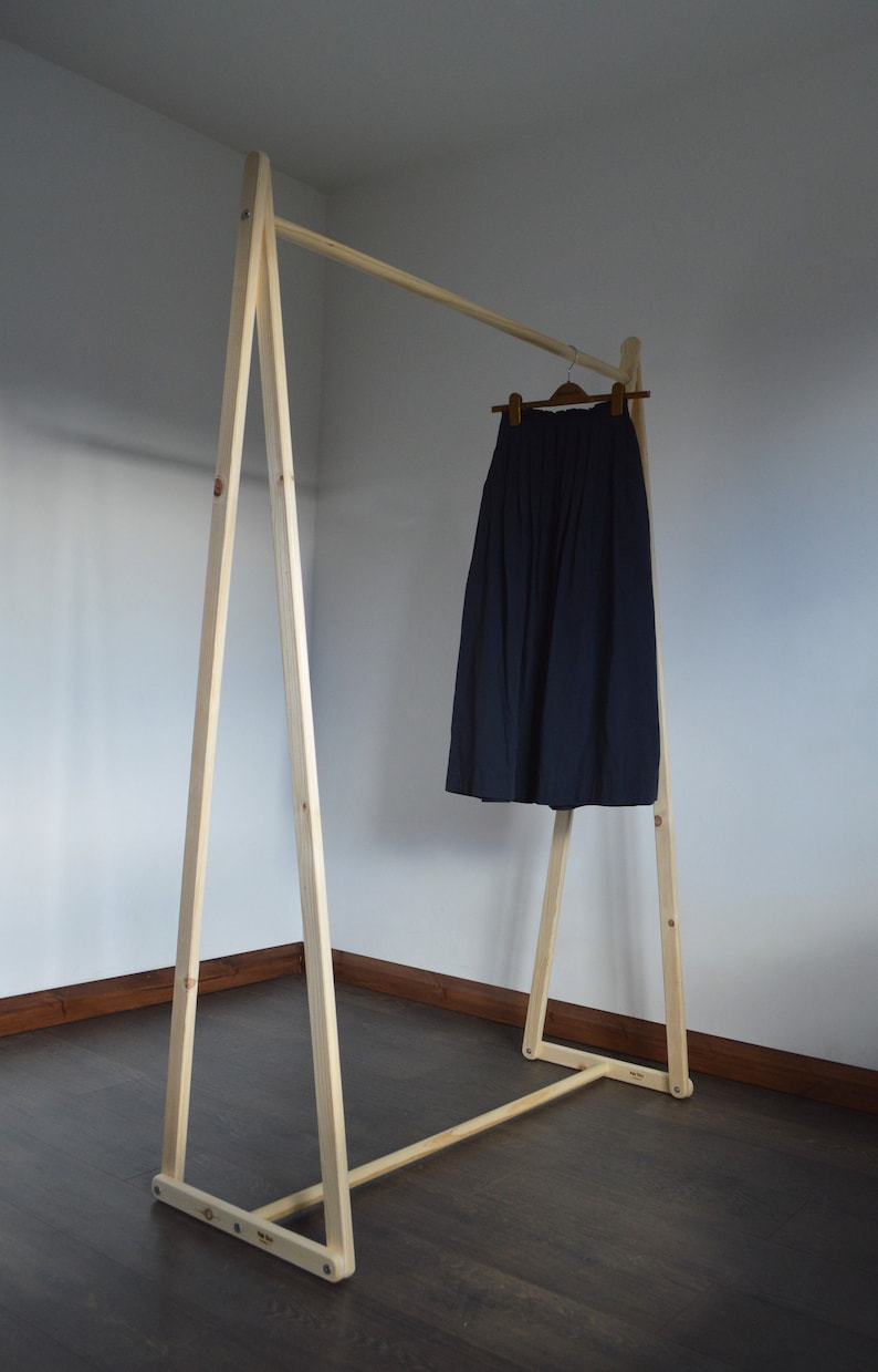 May include: A wooden clothing rack with a navy blue skirt hanging on a wooden hanger. The rack is made of light-colored wood and has a simple, minimalist design. The skirt is pleated and appears to be made of a soft fabric.