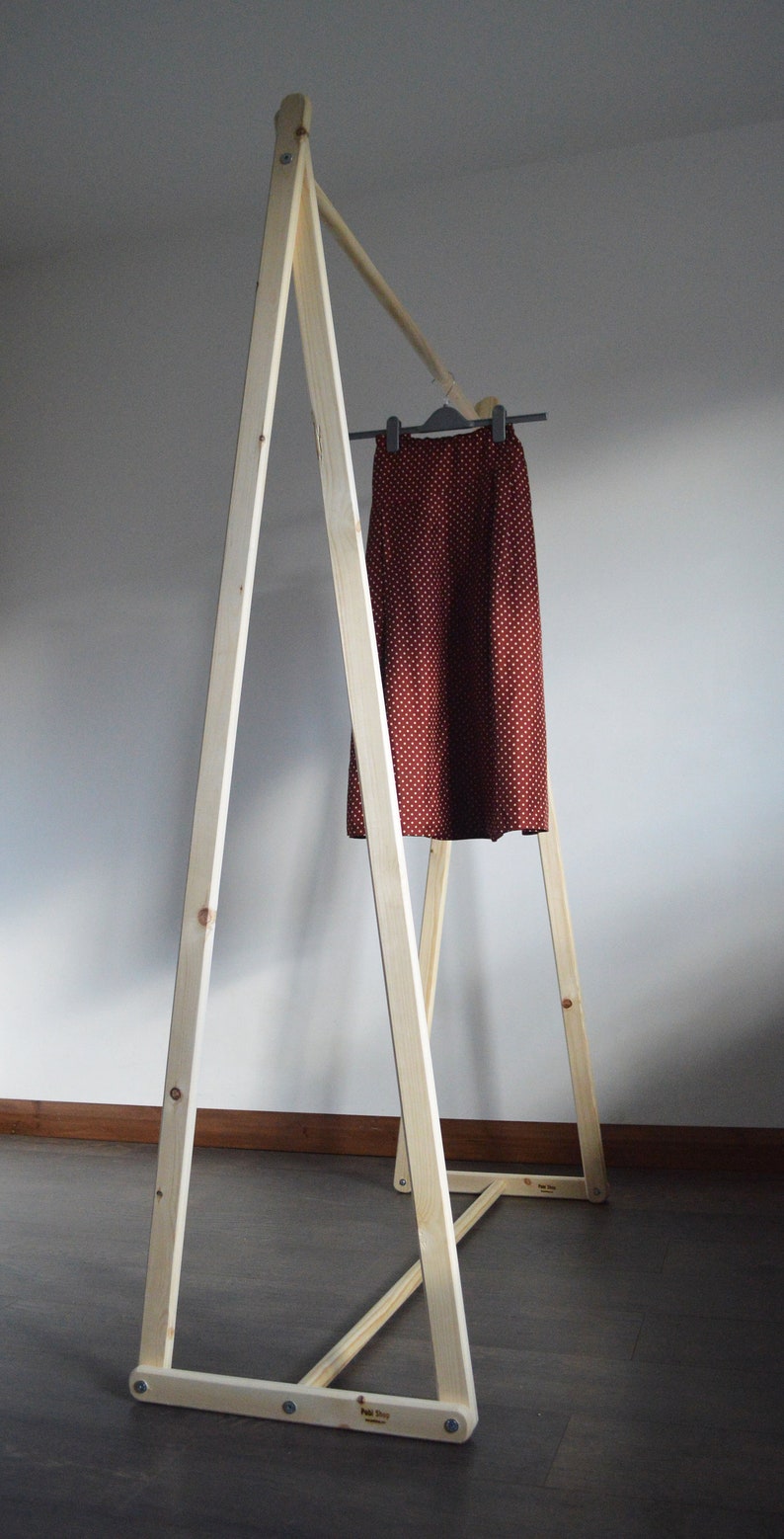 May include: A-frame wooden clothing rack with a skirt hanging on a hanger. The skirt is a dark red color with a white polka dot pattern. The rack is made of light-colored wood and is assembled with screws.