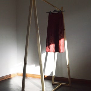 May include: A wooden clothing rack with a red skirt hanging on a hanger. The skirt has a white polka dot pattern. The rack is made of light-colored wood and is in a room with a dark wooden floor.