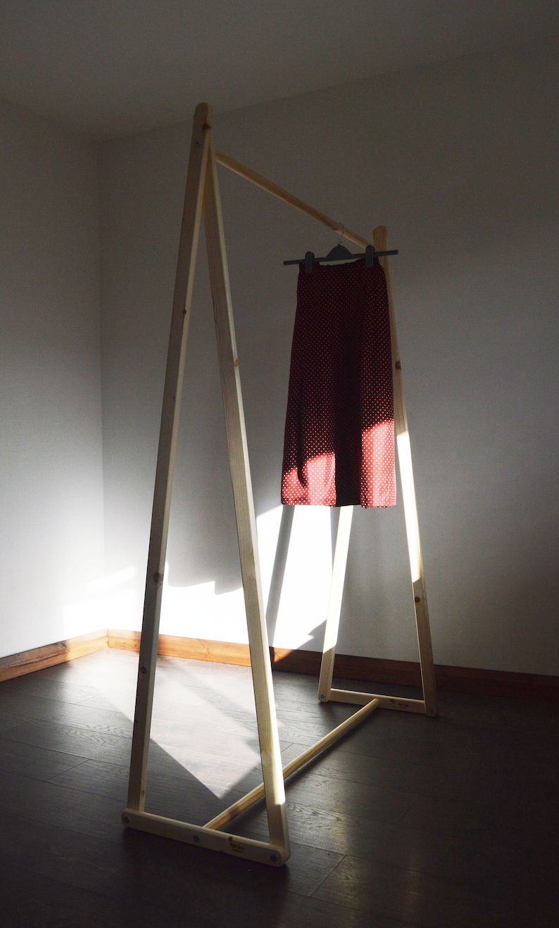 May include: A wooden clothing rack with a red skirt hanging on a hanger. The skirt has a white polka dot pattern. The rack is made of light-colored wood and is in a room with a dark wooden floor.