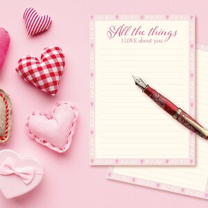 Può includere: Una collezione di articoli a tema San Valentino su sfondo rosa. Include decorazioni a forma di cuore in vari colori e motivi, una scatola regalo a forma di cuore, carta da lettere a righe con il testo "All the things I LOVE about you" e una penna stilografica rossa.