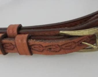 May include: A brown leather belt with a brass buckle and intricate floral designs. The belt is made from high-quality leather and has a classic western style.