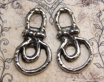 May include: Two silver metal pendants. Each pendant features a loop at the top, a textured section with small spheres, and a larger, open loop at the bottom. The pendants are shown against a patterned background.