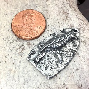 May include: A silver pendant featuring a detailed, textured design of a bird with outstretched wings. The pendant is shaped like a teardrop and has a hole at the top for attaching a chain.