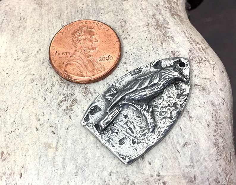 May include: A silver pendant featuring a detailed, textured design of a bird with outstretched wings. The pendant is shaped like a teardrop and has a hole at the top for attaching a chain.