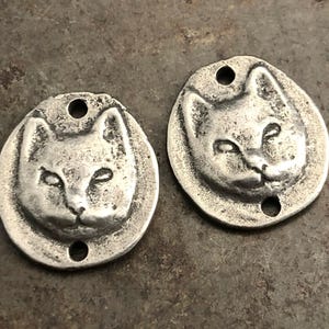 Può includere: Due ciondoli in metallo argentato a forma di viso di gatto. Ogni ciondolo ha due fori per attaccarlo a gioielli o altri oggetti artigianali.