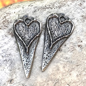 May include: Two silver heart-shaped charms with a textured surface and a hole at the top for attaching to jewelry.