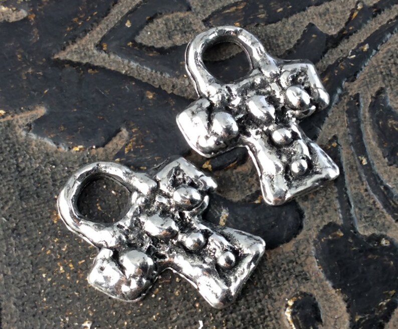 Puede incluir: Dos encantos Ankh de plata con un acabado texturizado. Los encantos tienen un bucle en la parte superior para sujetarlos a un collar o pulsera.