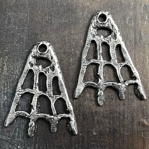May include: Two silver metal pendants shaped like a triangle with a web-like design. The pendants have a hole at the top for hanging.