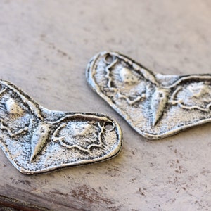 May include: Two silver metal charms shaped like a butterfly with a textured surface.
