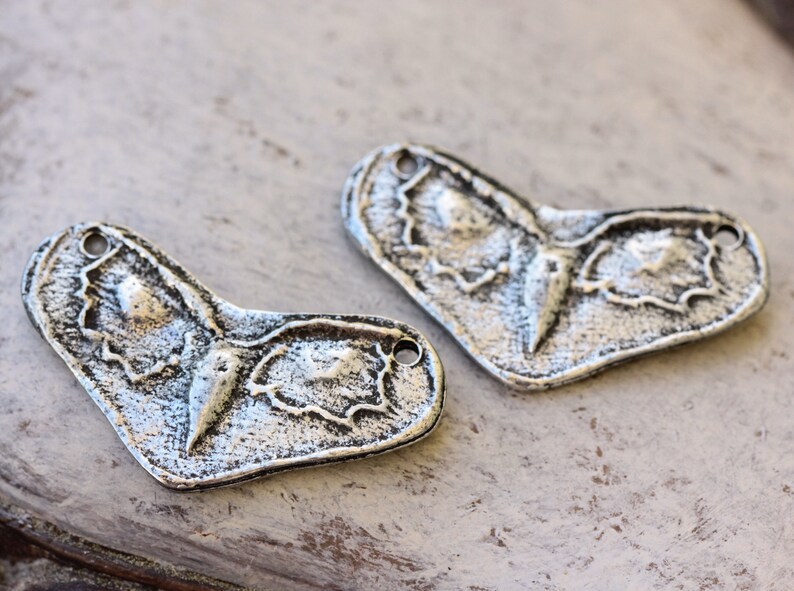 May include: Two silver metal charms shaped like a butterfly with a textured surface.