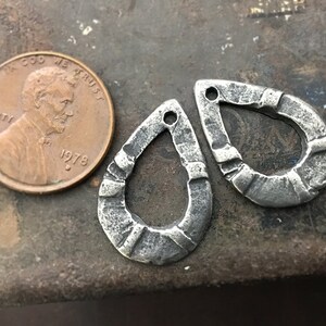 Puede incluir: Dos colgantes de metal plateado en forma de l&aacute;grima con un aspecto texturizado y martillado. Cada colgante tiene un peque&ntilde;o agujero en la parte superior para ensartar. Se incluye una moneda de un centavo estadounidense de 1978 para comparar el tama&ntilde;o.