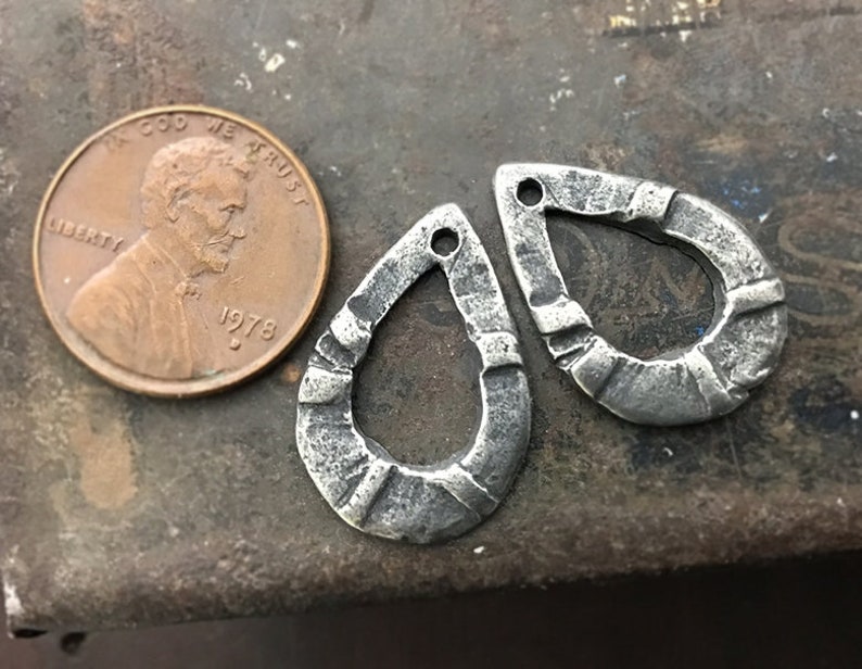 Puede incluir: Dos colgantes de metal plateado en forma de l&aacute;grima con un aspecto texturizado y martillado. Cada colgante tiene un peque&ntilde;o agujero en la parte superior para ensartar. Se incluye una moneda de un centavo estadounidense de 1978 para comparar el tama&ntilde;o.