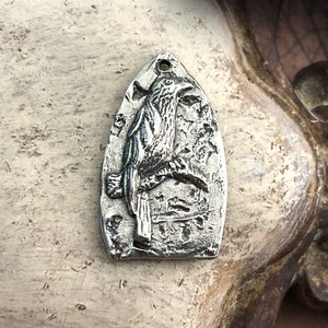 May include: A silver charm in the shape of a bird with detailed etching. The charm is shaped like a teardrop and has a loop at the top for attaching to a necklace or bracelet.