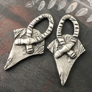 May include: Two silver metal earrings with a geometric design. Each earring features a loop and a pointed shape with a textured surface.